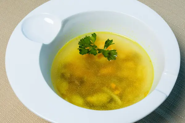 Caldo de pollo casero dorado con perejil en un cuenco blanco