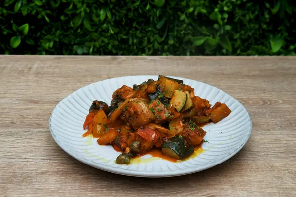 Pisto manchego de verduras guisadas en un plato blanco sobre madera